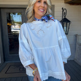 woman in white eyelet detail blouse outside with gold jewelry and satin coloirful scarf fall blouse 