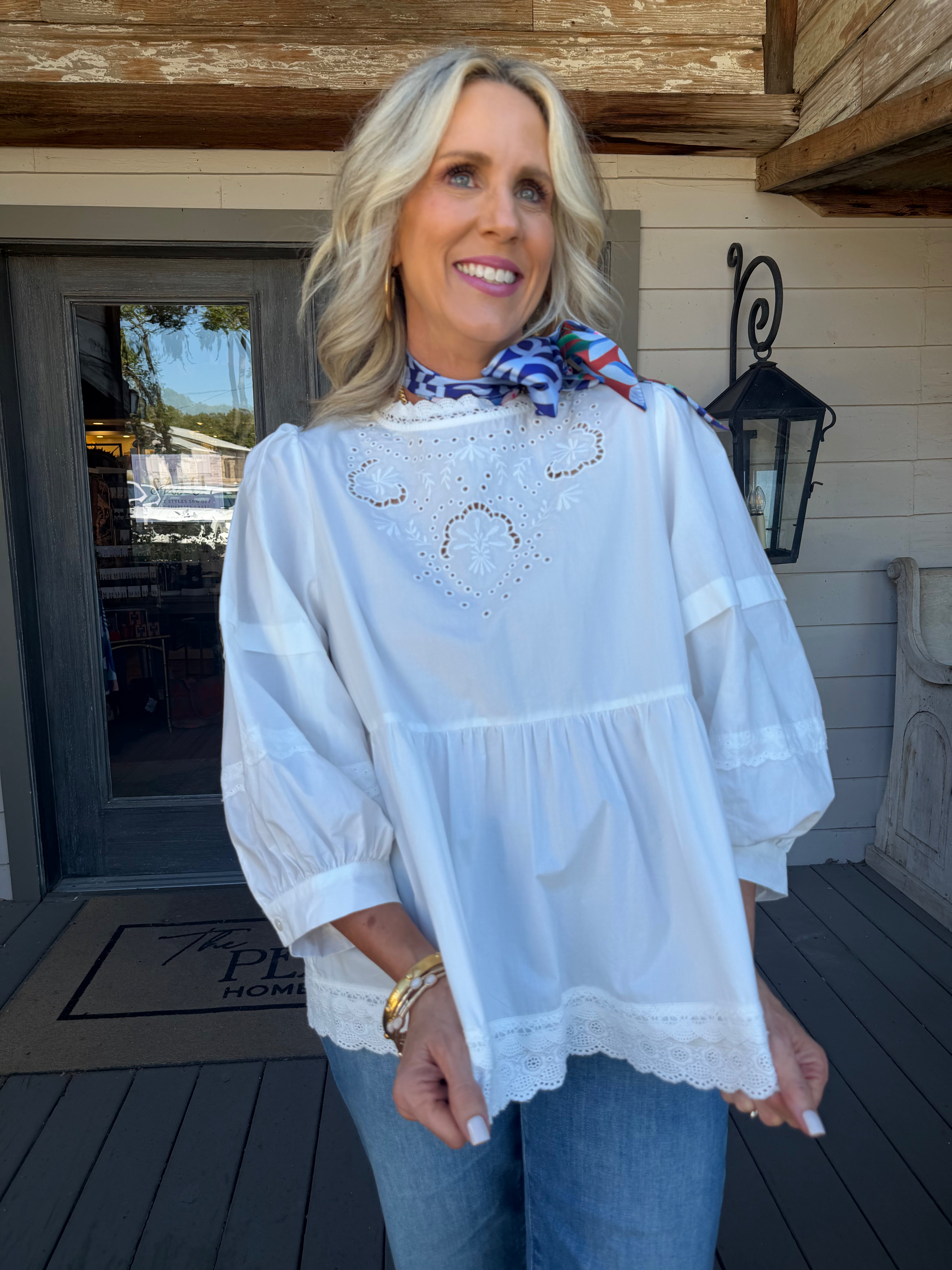 woman in white eyelet detail blouse outside with gold jewelry and satin coloirful scarf fall blouse 