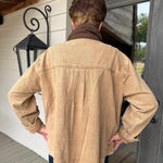 A person viewed from behind wearing a tan canvas utility jacket with a brown collar, standing on a porch in front of a dark gray door.