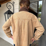 A person viewed from behind wearing a tan canvas utility jacket with a brown collar, standing on a porch in front of a dark gray door.