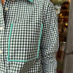 A close-up of a person wearing a green and white gingham check long-sleeve button-up shirt with contrasting mint green piping around the collar and chest pocket.