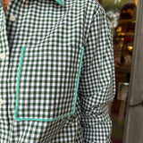 A close-up of a person wearing a green and white gingham check long-sleeve button-up shirt with contrasting mint green piping around the collar and chest pocket.
