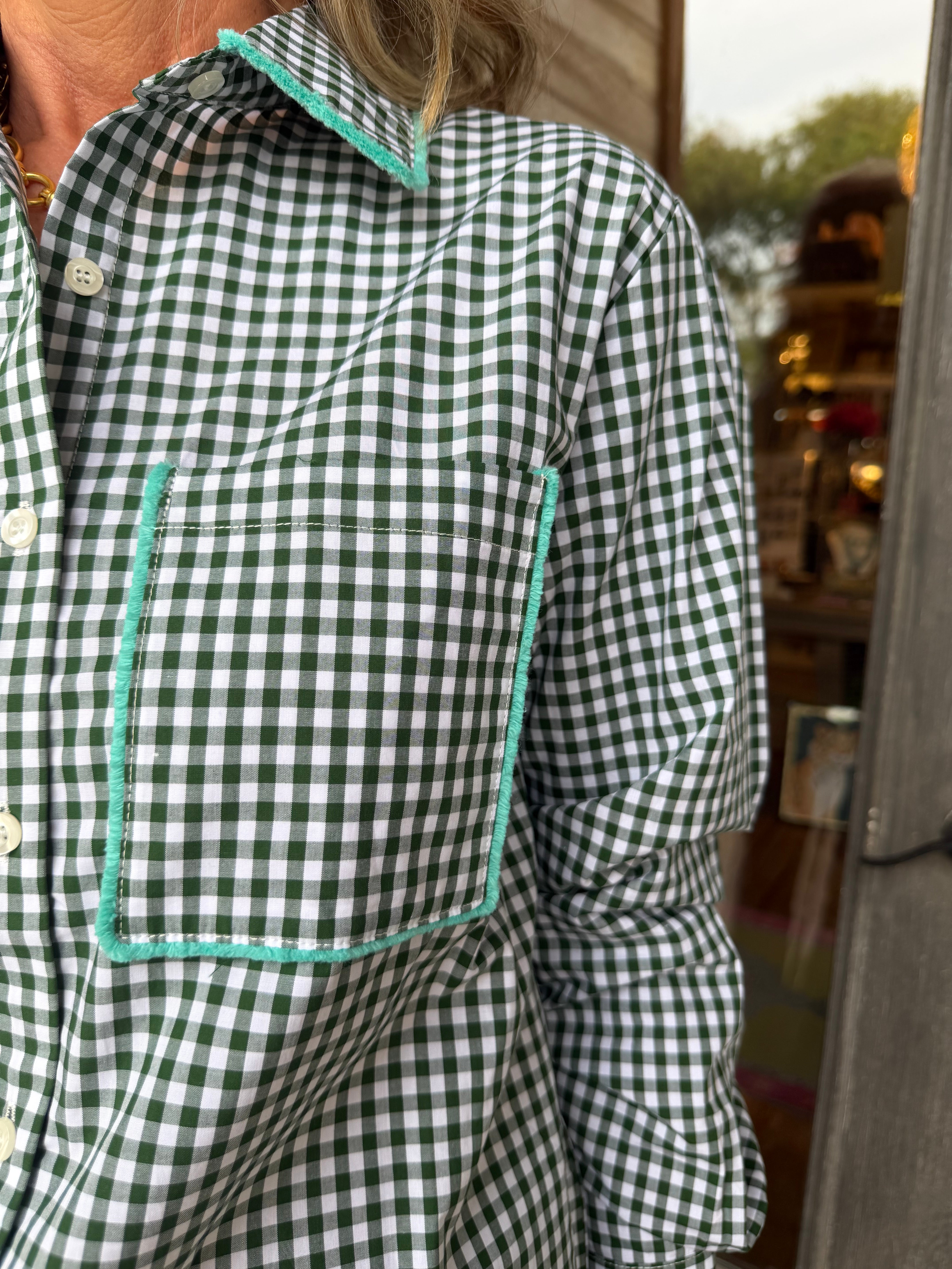 A close-up of a person wearing a green and white gingham check long-sleeve button-up shirt with contrasting mint green piping around the collar and chest pocket.